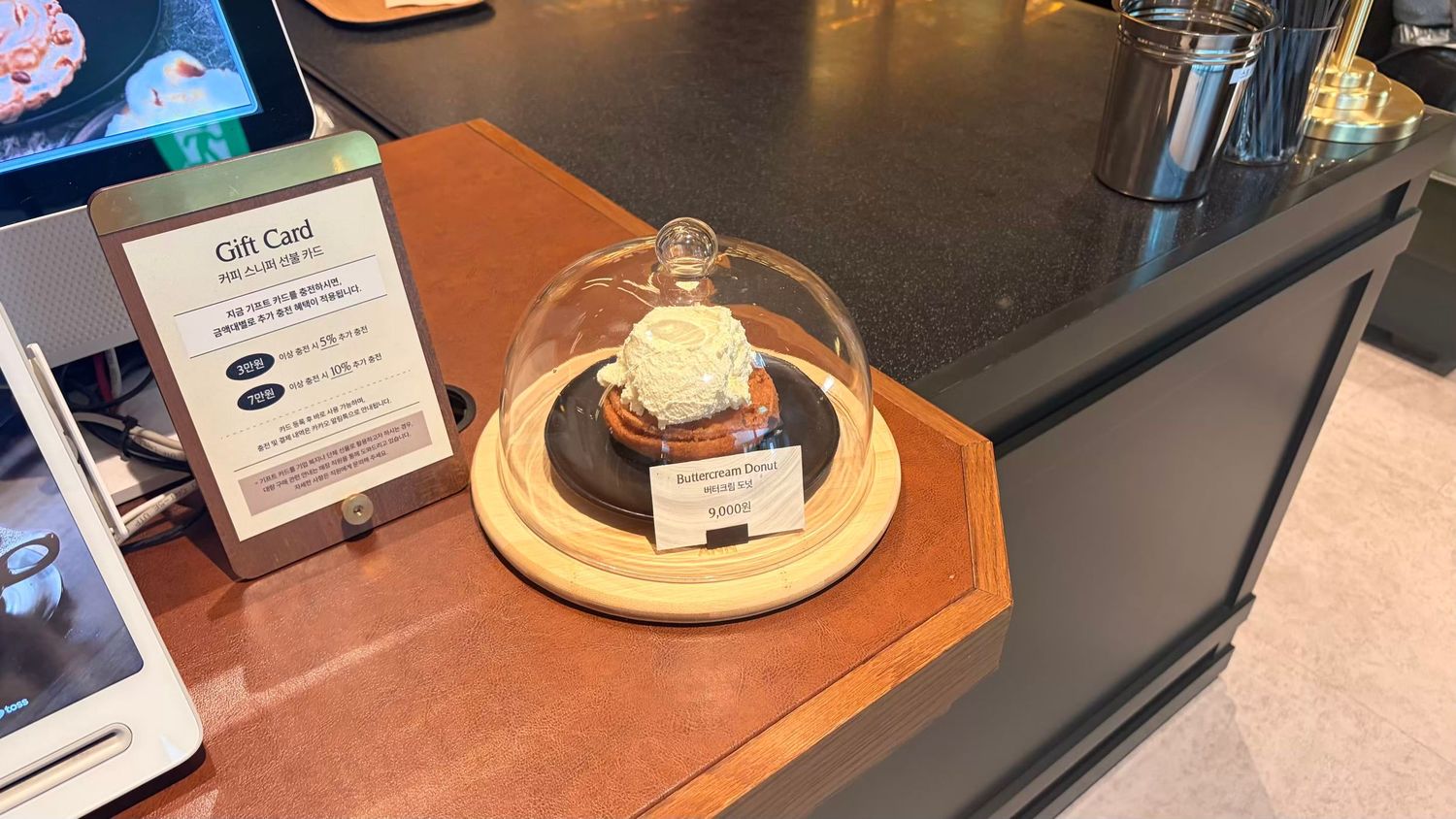 A decorative white rose displayed under a glass cloche dome on a wooden base at a gift card display counter.