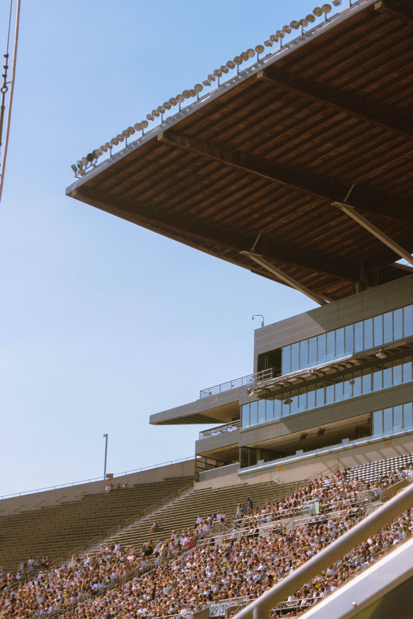 Packed stadium grandstand with crowds of spectators under a clear blue sky during a sporting event.