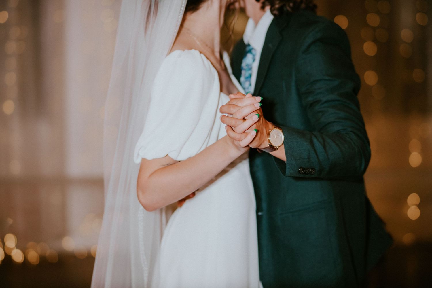 A bride in a white gown and veil shares a first dance with a groom in a dark green suit at a wedding reception.