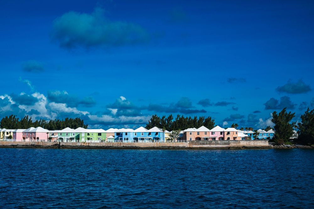 Colorful pastel waterfront homes line the shore of a tropical island under a vivid blue sky in Bermuda.