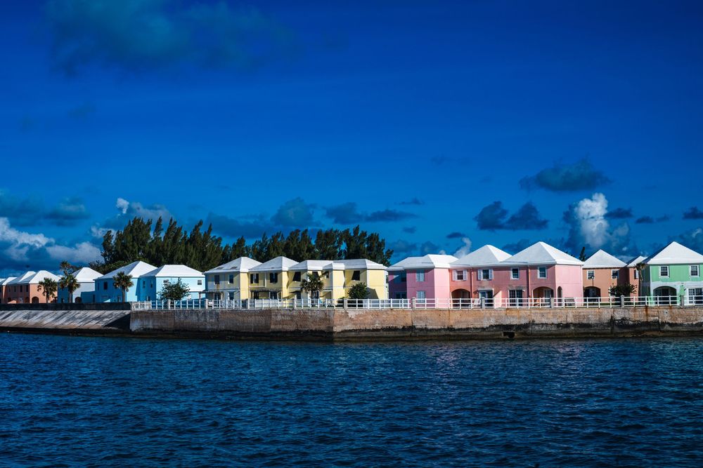 Colorful pastel waterfront cottages line the rocky shore under a vivid blue sky in Bermuda.