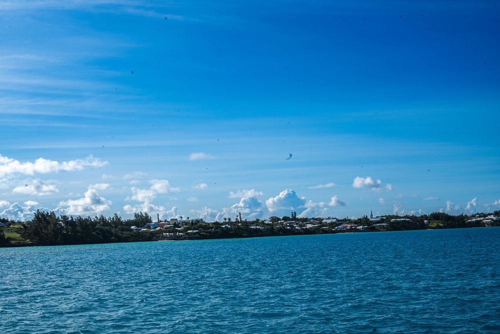 Turquoise ocean waters with a lush green coastline under a vibrant blue sky with white clouds in Bermuda.