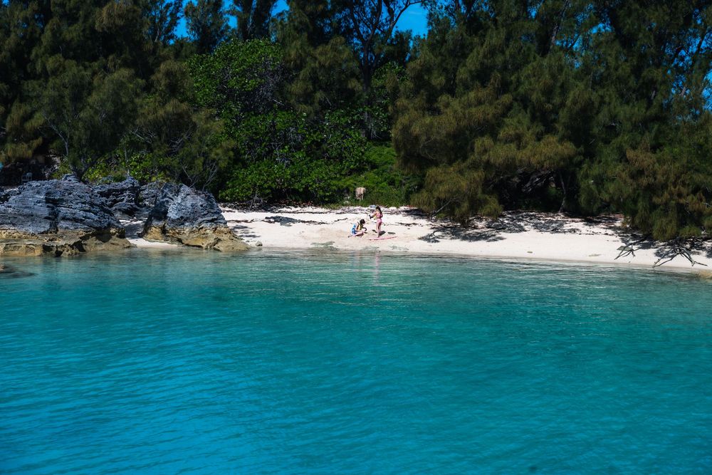 Turquoise waters lap against a pristine white sand beach with lush green trees and rocky outcrops in a tropical paradise.