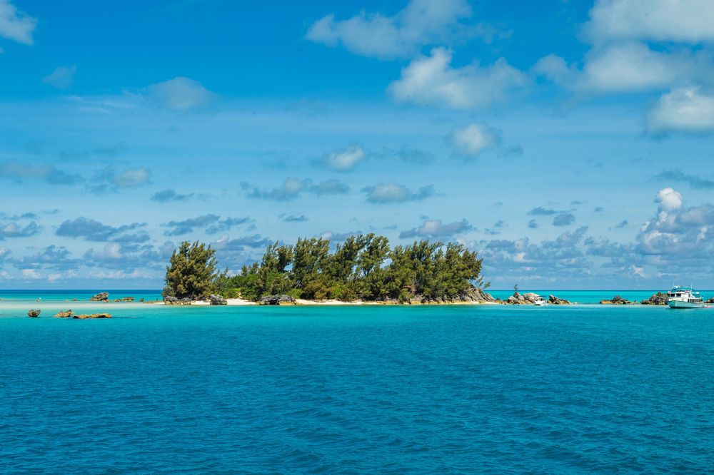 Small tropical island with lush green trees and white sandy beach surrounded by turquoise Caribbean waters under blue sky.