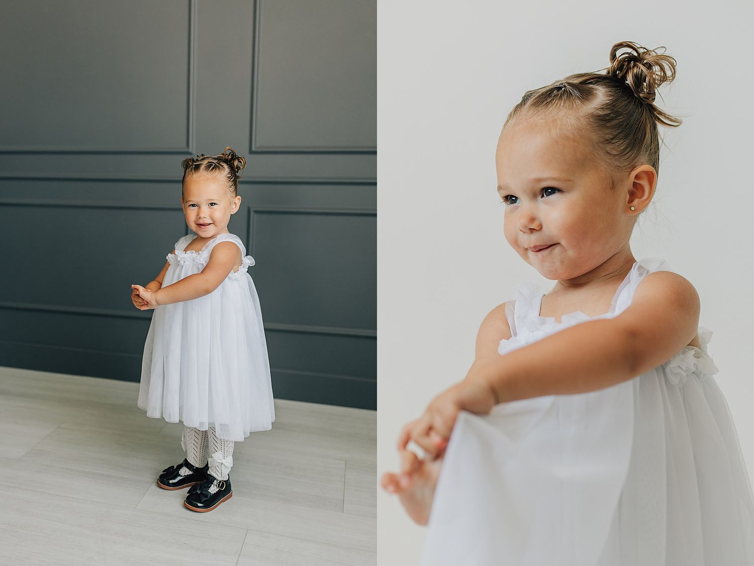 A toddler girl in a white tulle dress with a bun hairstyle smiles and plays in a modern studio.
