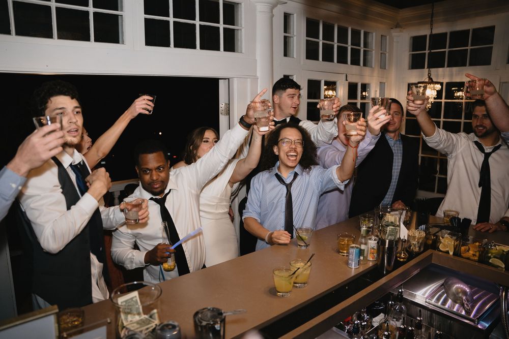 Group of guests raising glasses in a toast at a wedding reception bar, celebrating with drinks and smiles.