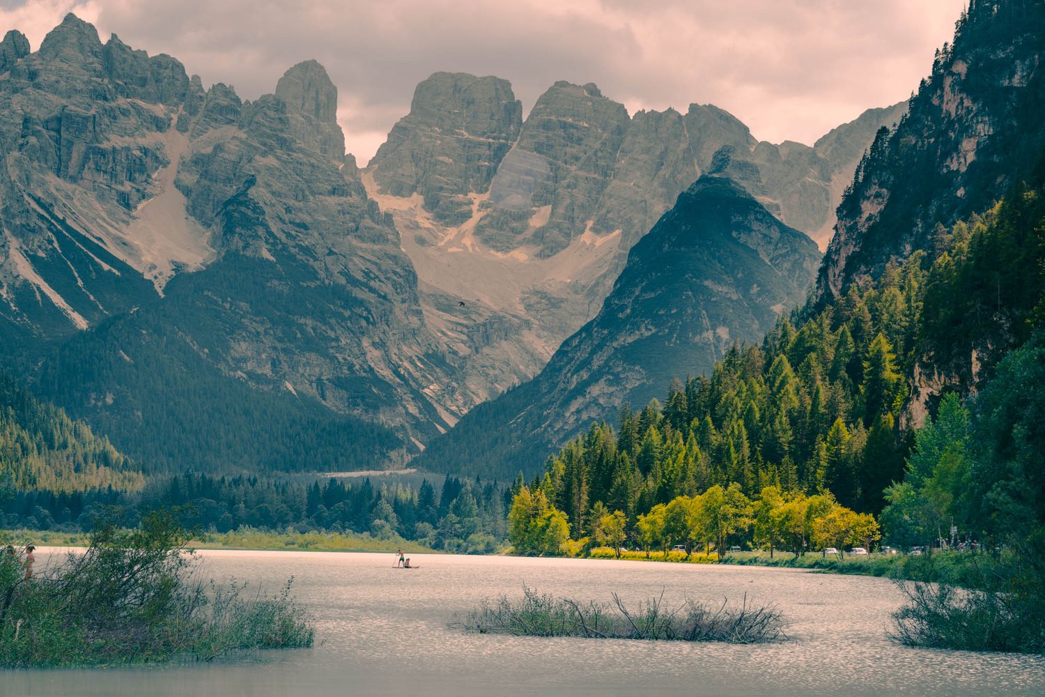 Dramatic Dolomite mountains with jagged rocky peaks, winding road, and moody overcast sky in the Italian Alps.