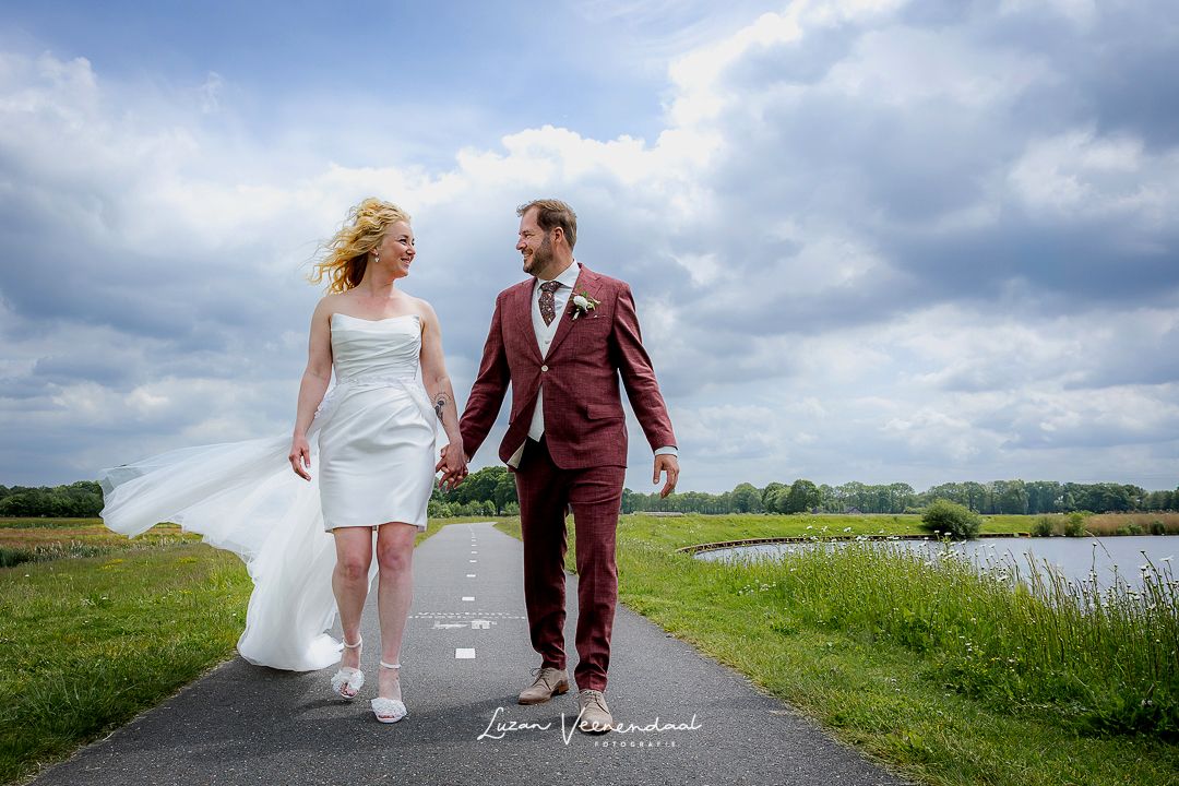 Vincent en Madelief wandelen hand in hand over een fietspad omringd door water en groen, kijkend naar elkaar