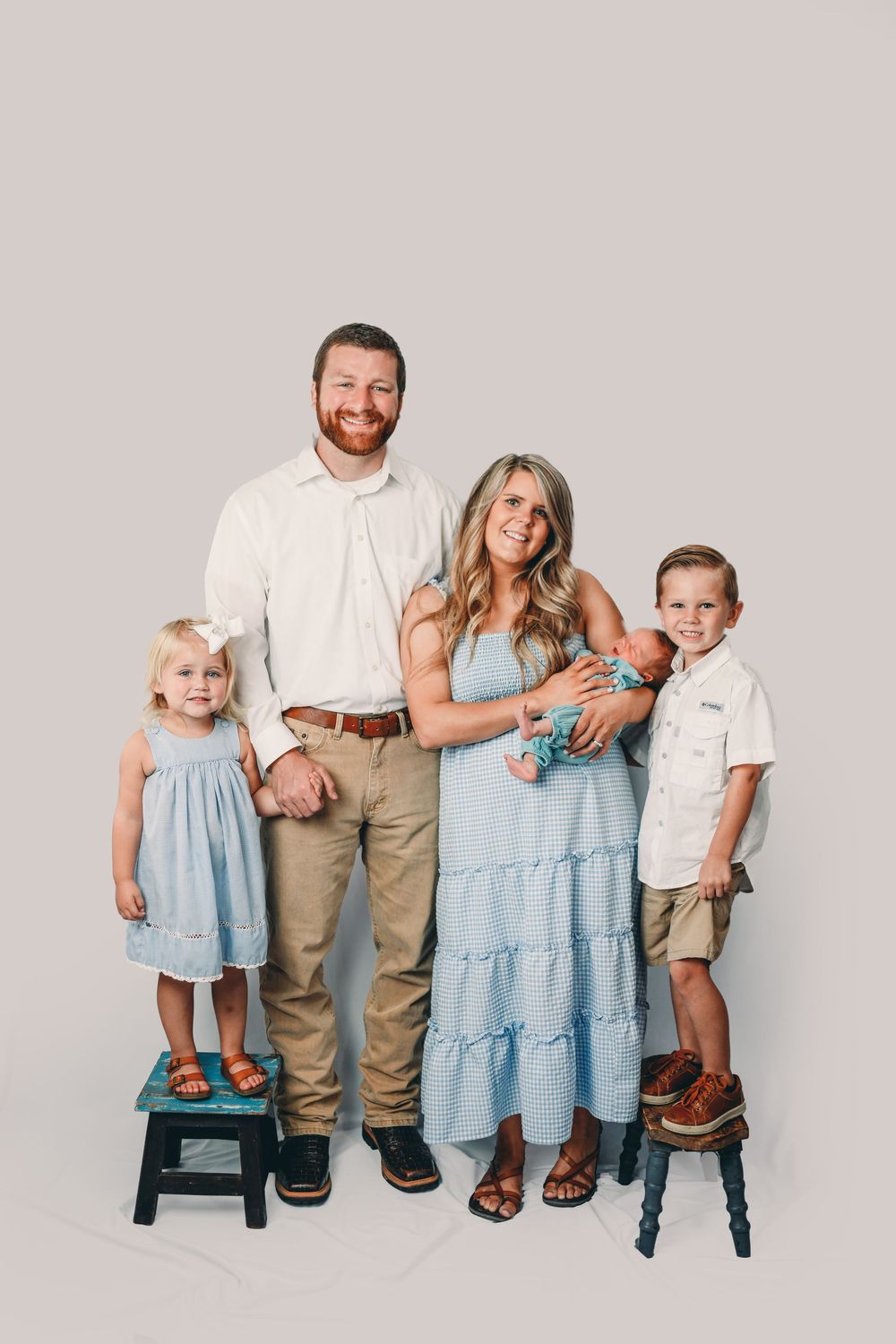 Family portrait of parents with three children, including a newborn, dressed in coordinating blue and neutral tones.