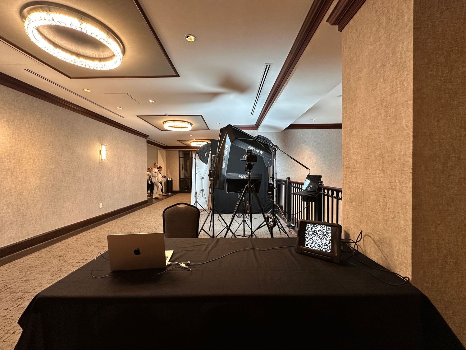 Professional dance photography studio setup with lighting equipment, laptop, and camera on black draped table in hotel corridor.