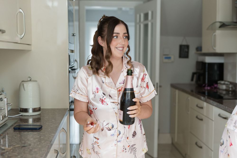 Woman in floral robe holding a wine bottle in a modern kitchen, smiling happily.