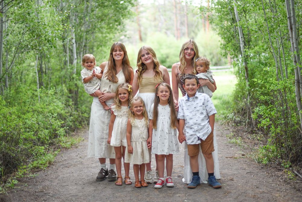 Family group photo of adults and children smiling on a forest path surrounded by lush green trees.
