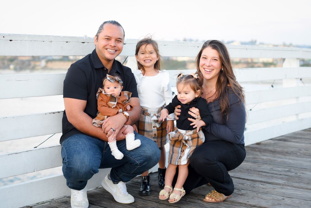 Happy family of five posing on a white pier, parents crouching with three young children on a sunny day.