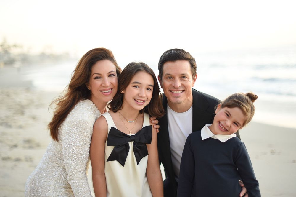 Happy family of four smiling together on a sunny beach, dressed in elegant white and navy outfits.