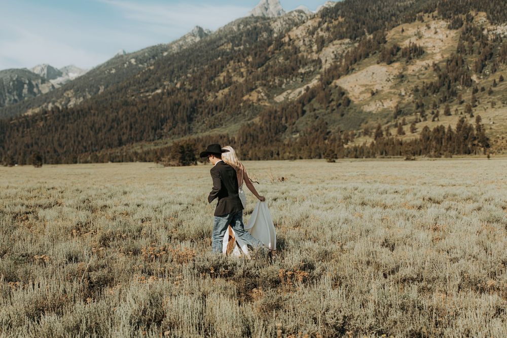 Couple walking through a mountain meadow in Grand Teton National Park, bride in flowing white dress.