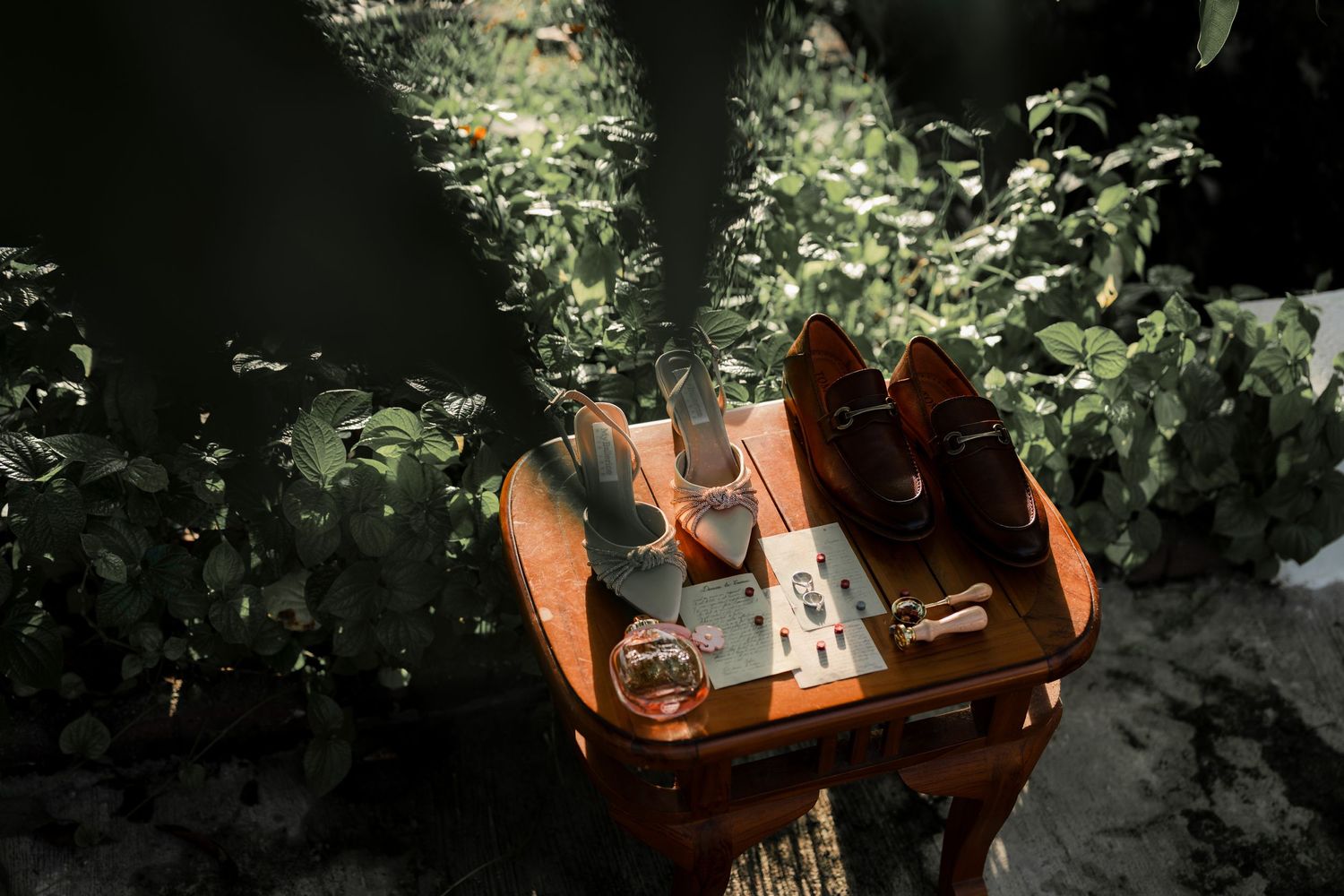 A wooden table in a garden setting with wedding details and sunlight filtering through.