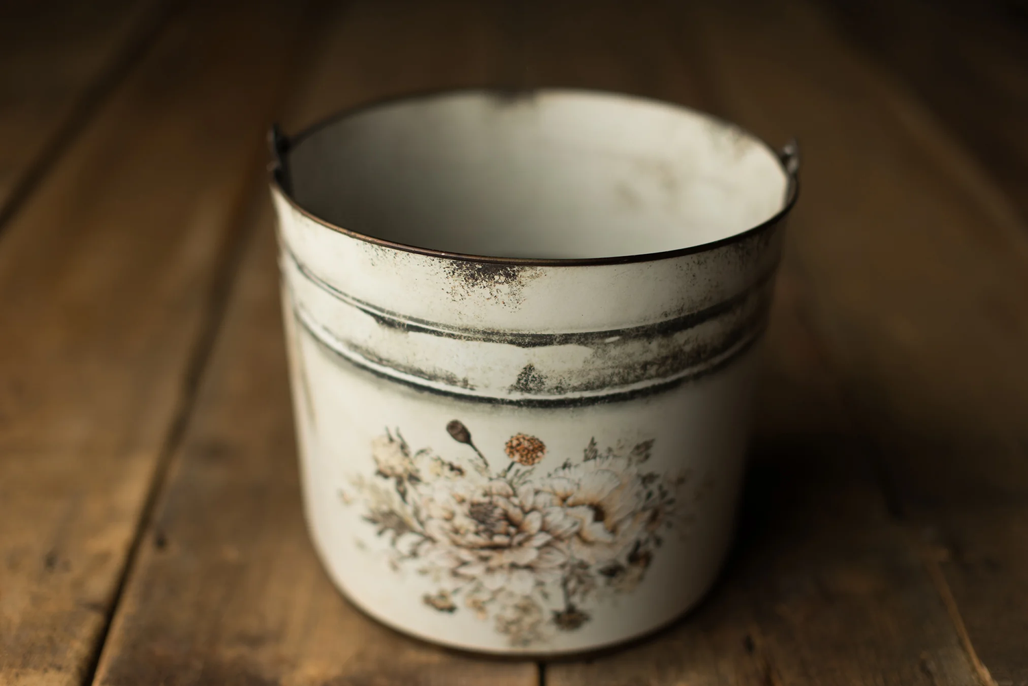 Vintage white enamel bucket with floral rose design on wooden surface.