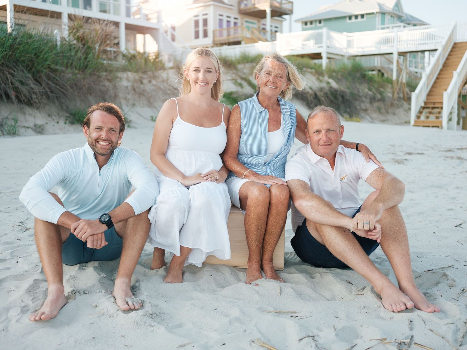 Two adults and two older adults posing together on beach with coastal homes in background.