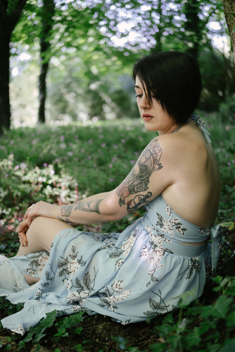 Portrait féminin en forêt mettant en valeur les tatouages et la lumière naturelle.