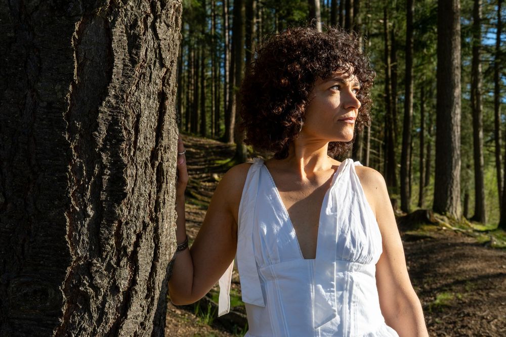 Portrait féminin en forêt, éclairé par la lumière naturelle entre les arbres.