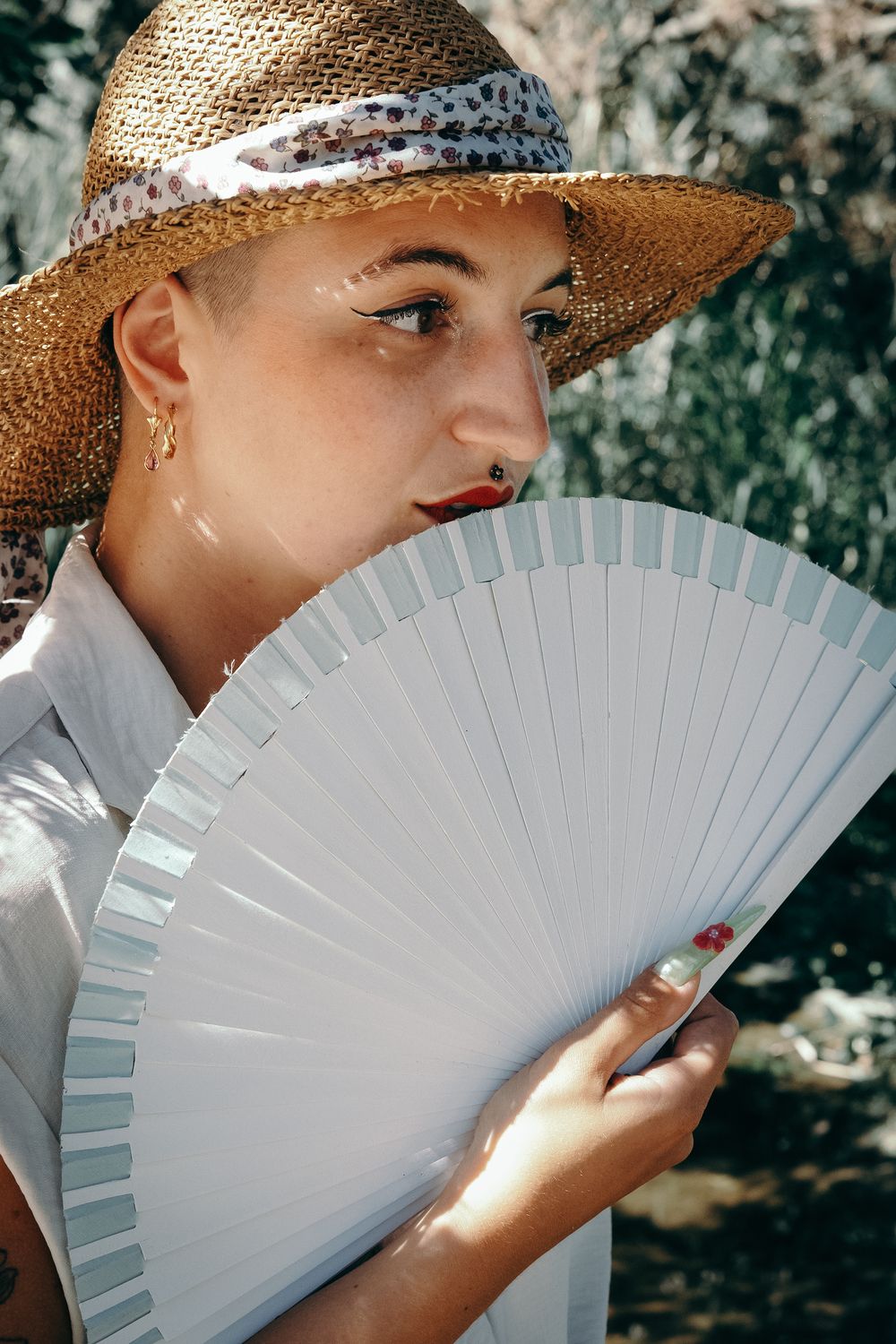 Portrait féminin en extérieur près de Lyon avec chapeau de paille et éventail en lumière naturelle.