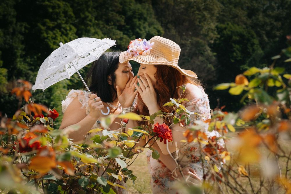 Portrait de deux femmes en robes fleuries partageant un moment complice au milieu d’un jardin fleuri.