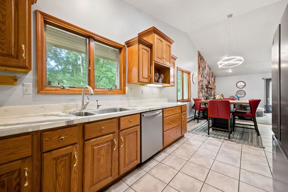 Bright kitchen featuring oak cabinets, marble countertops, stainless dishwasher, and open view to dining area.