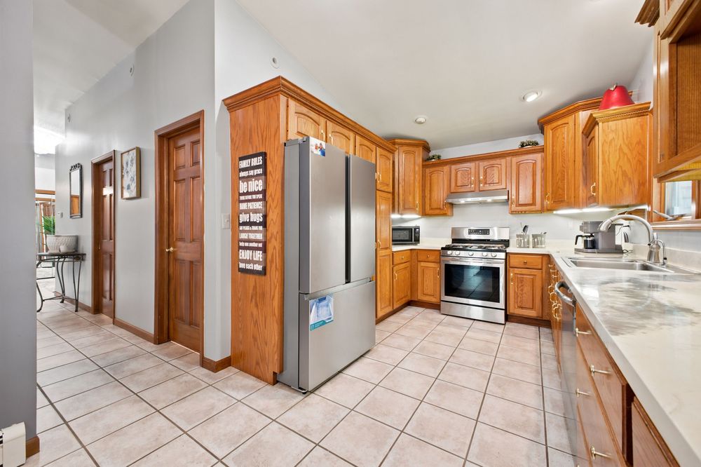 Spacious kitchen with stainless steel appliances, oak cabinets, light tile flooring, and a sink with window view.