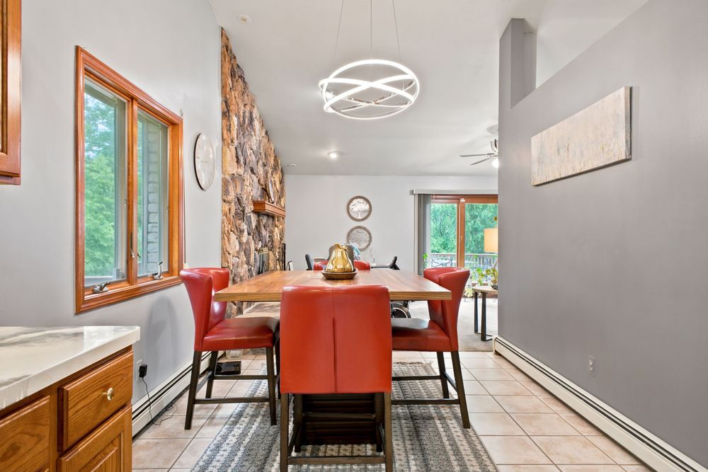 Bright dining room with red leather chairs, wood table, modern chandelier, stone accent wall, and tile flooring.