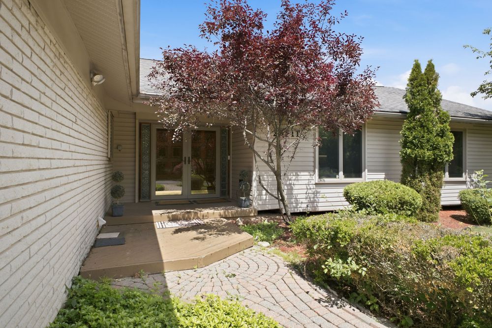 Brick ranch home entrance with decorative red maple tree, curved paver walkway, and manicured shrubs in a welcoming front courtyard.