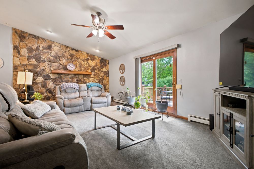 Cozy living room with stone accent wall, gray sectional sofa, ceiling fan, coffee table, and sliding glass doors to a deck.