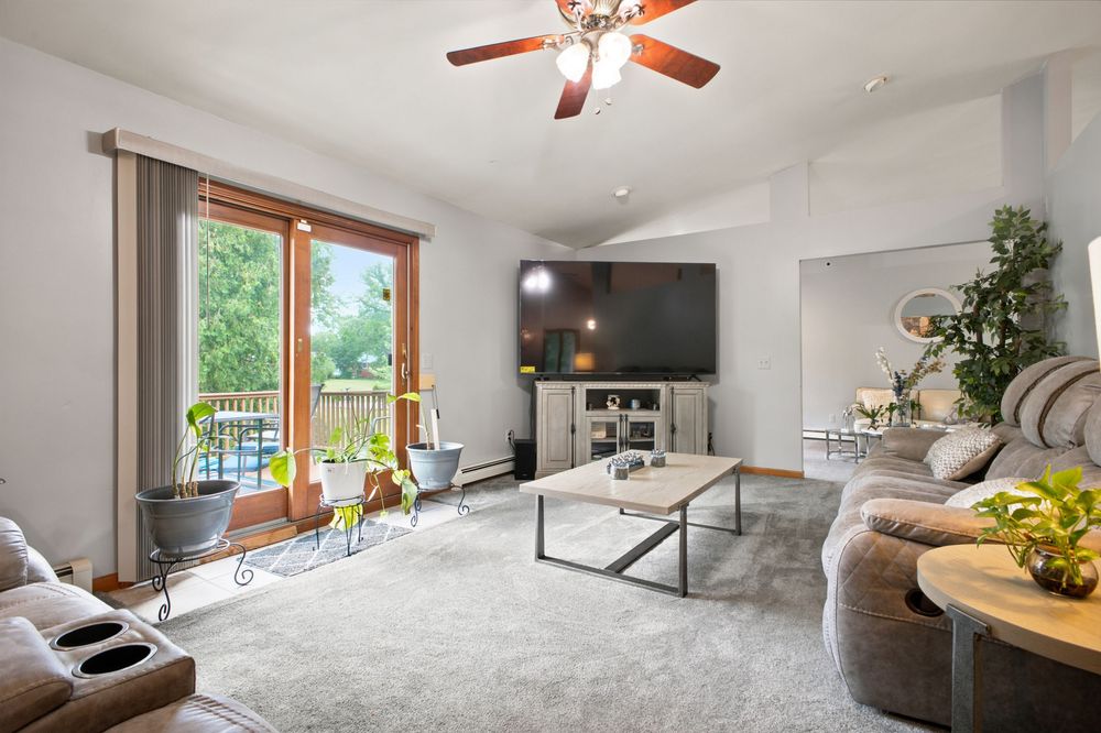Bright living room with ceiling fan, large TV, glass door to balcony, and comfortable sectional sofa.