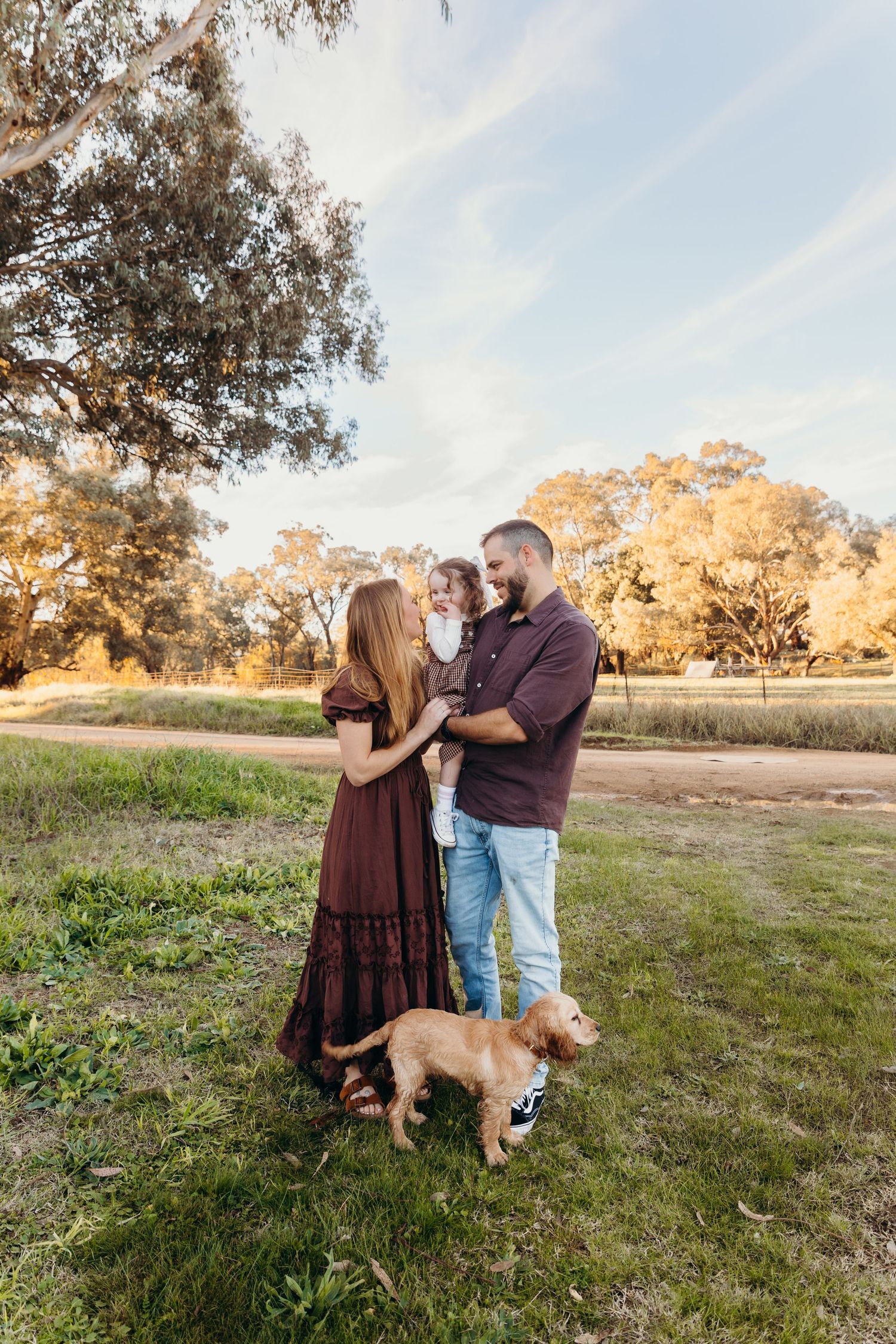 A happy family with a golden cocker spaniel dog standing together on green grass during a warm sunset.