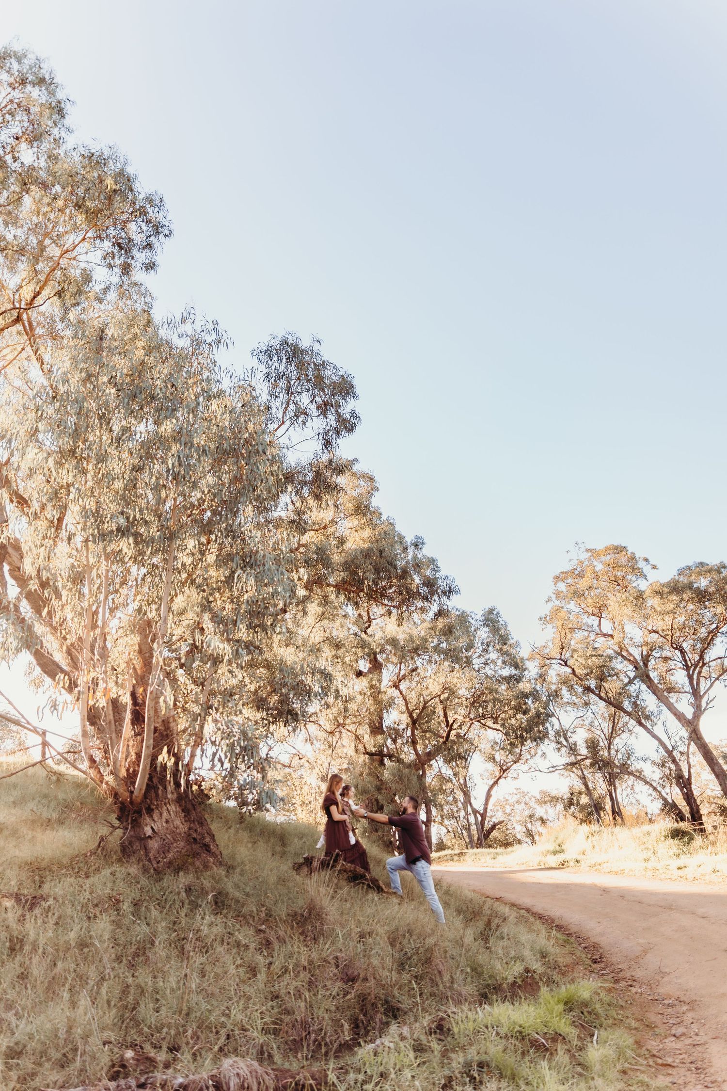 A couple laughs together near large eucalyptus trees along a rural dirt road.