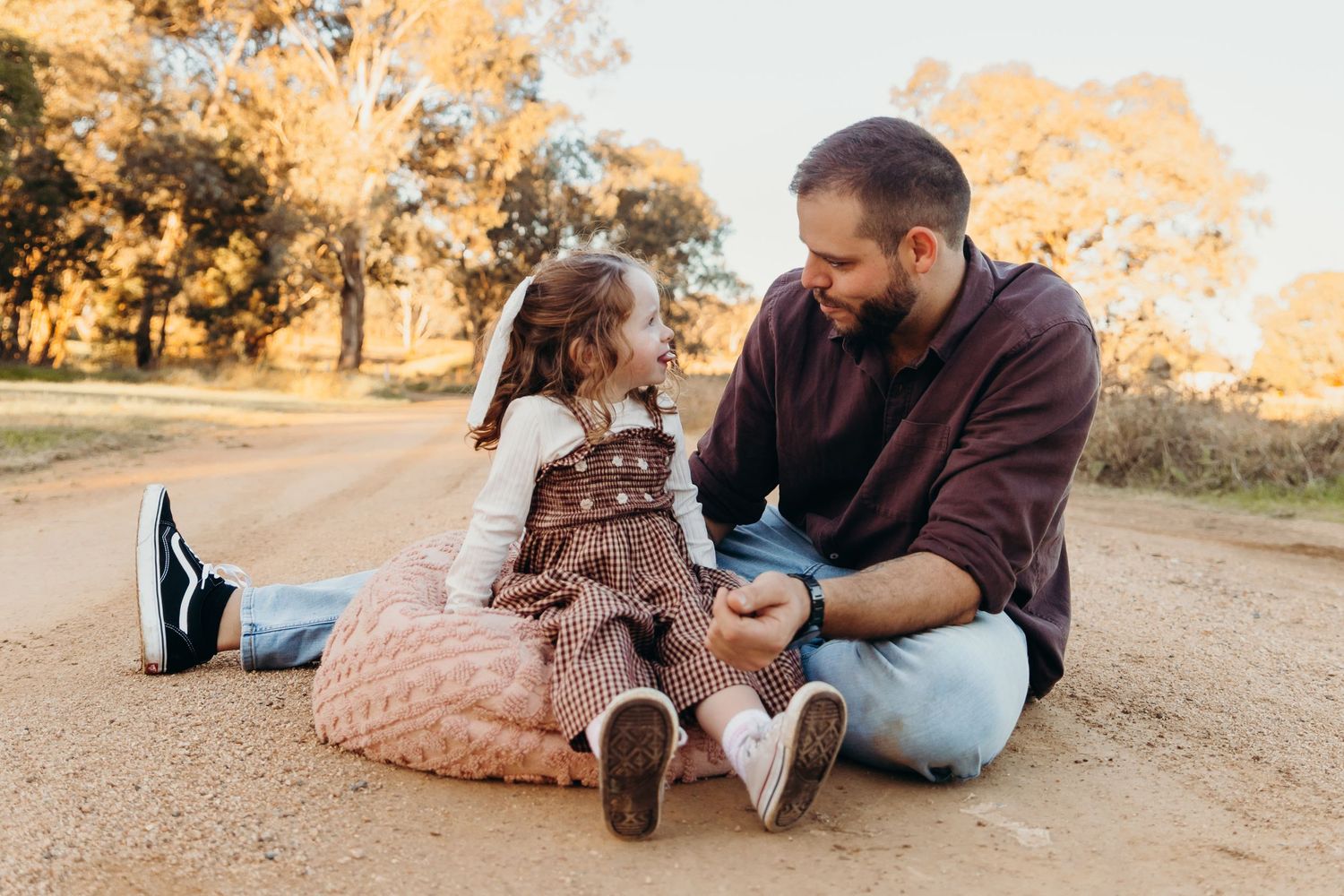 Father and daughter sitting together on a sunny dirt road.
