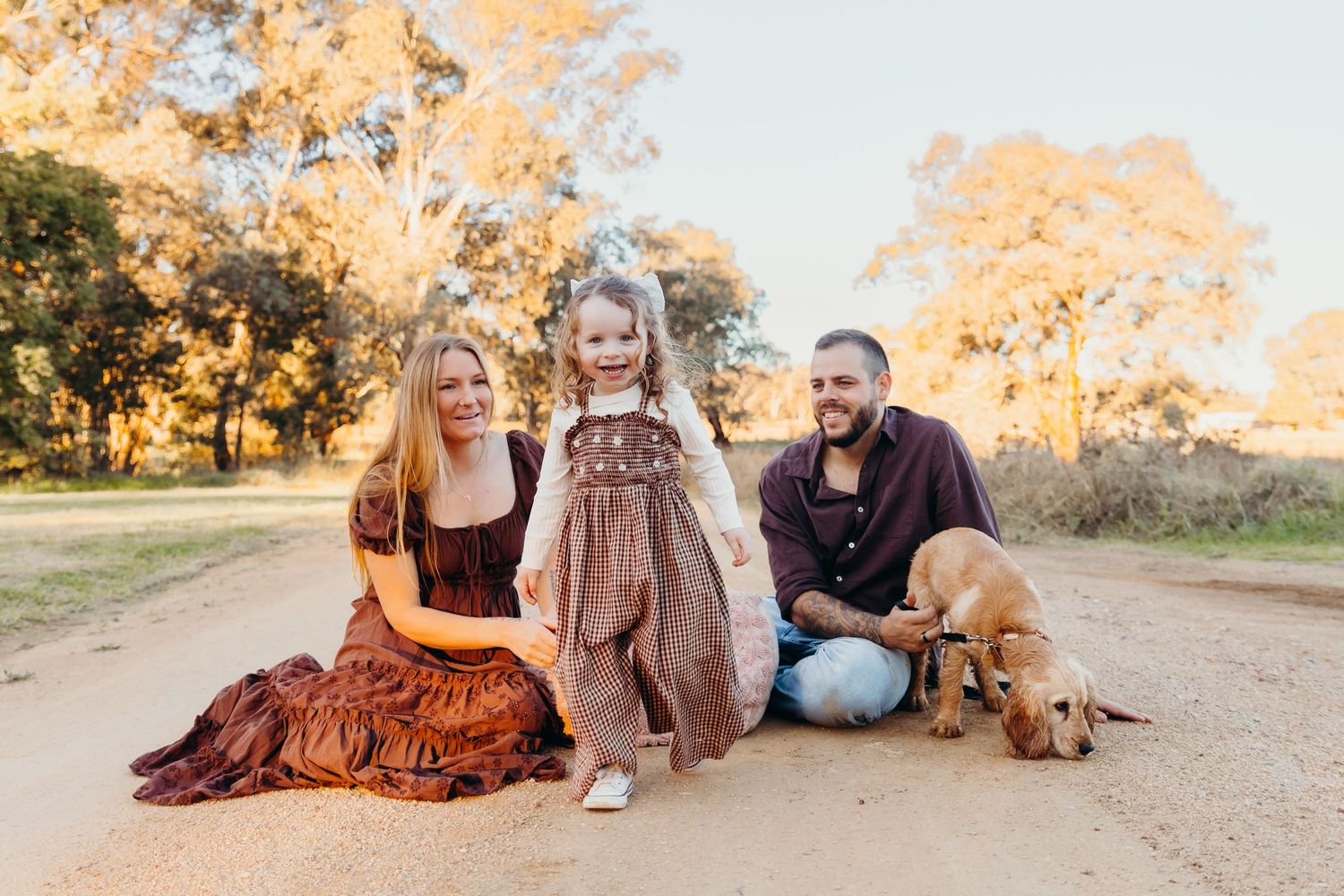Happy family with toddler and golden dog on a sunny dirt road.