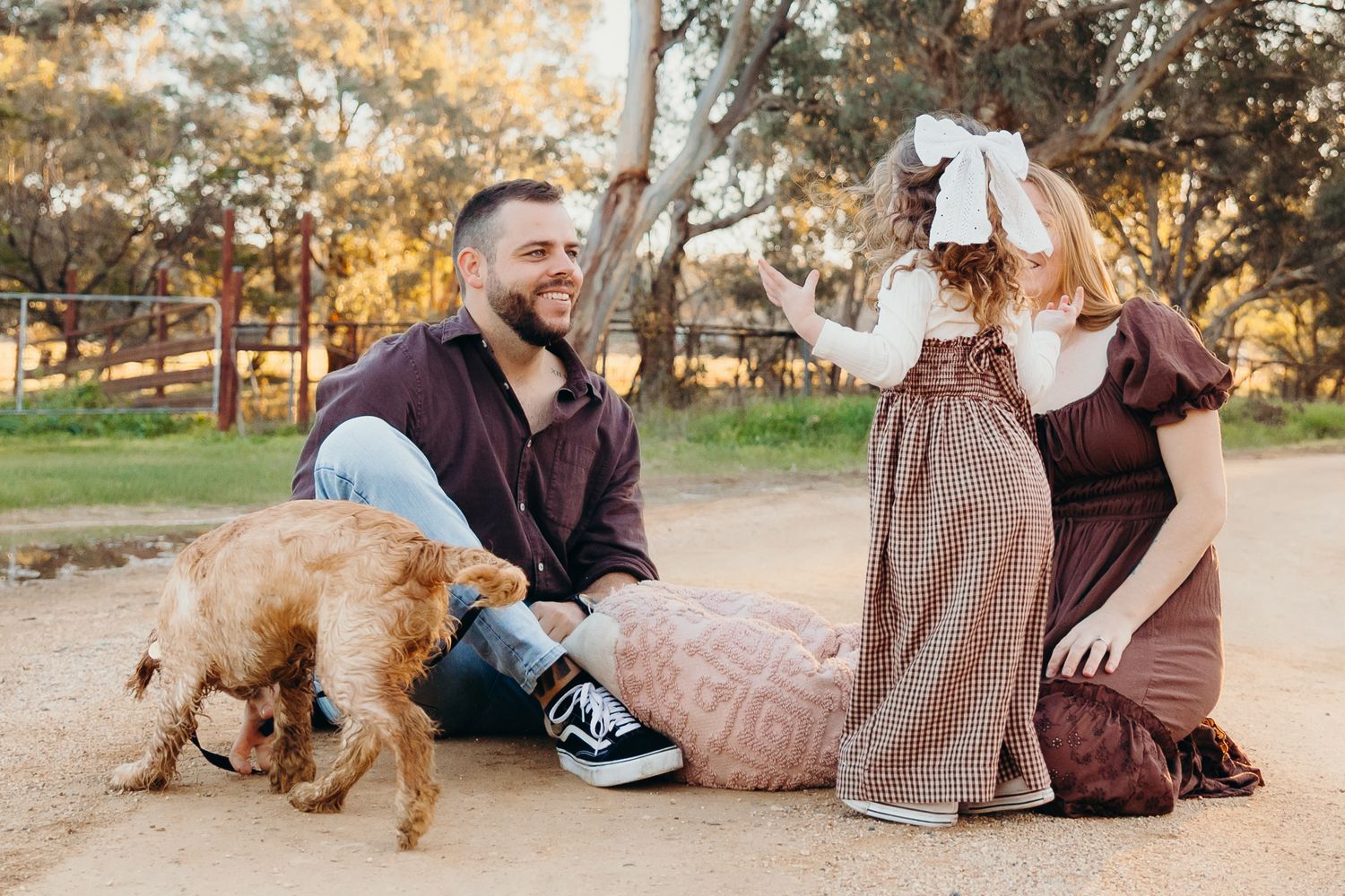 Family sitting on dirt road with fluffy dog in autumn park.