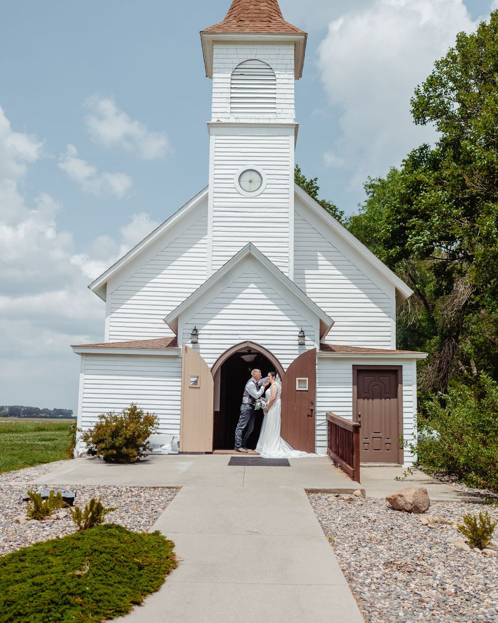 Bride and groom kissing in the doorway of a charming white rural chapel on a sunny day.