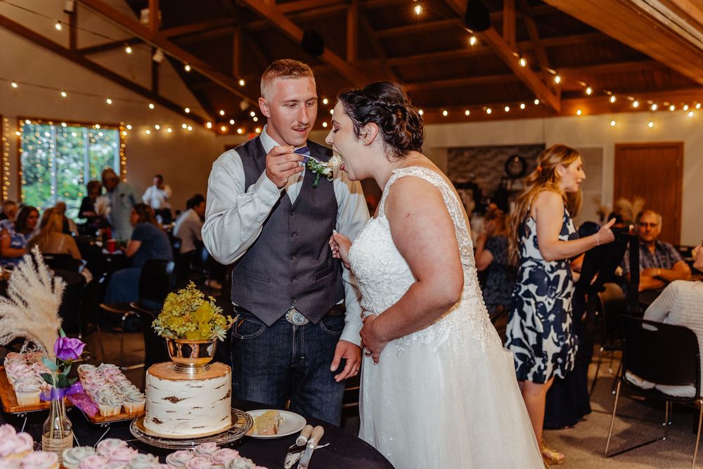 Bride and groom cut their rustic wedding cake at a reception with string lights and guests nearby.