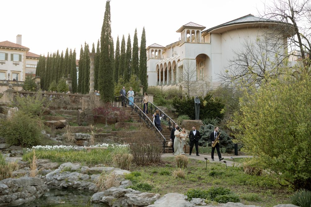 Wedding party walks through lush garden grounds of stunning Italian-style mansion wedding venue.