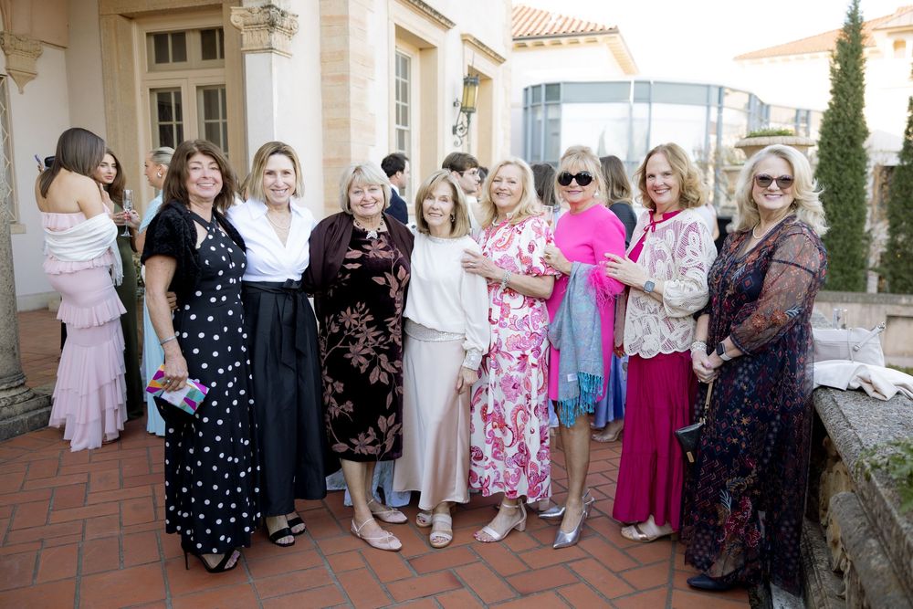 Group of elegantly dressed women smiling together on terrace at outdoor wedding reception.