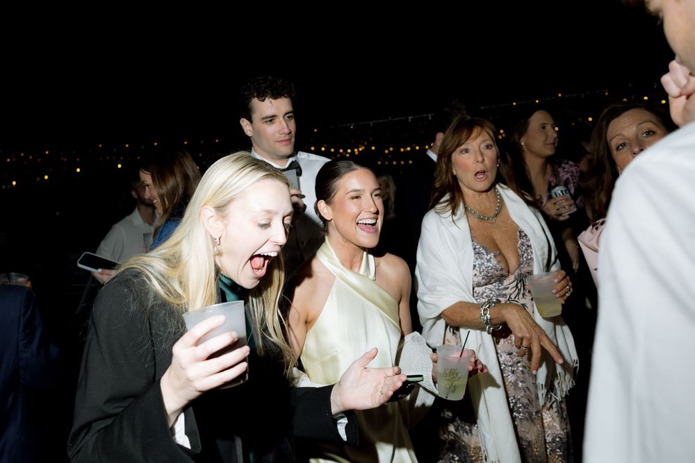 Excited wedding guests laughing and celebrating together during lively outdoor evening reception party.