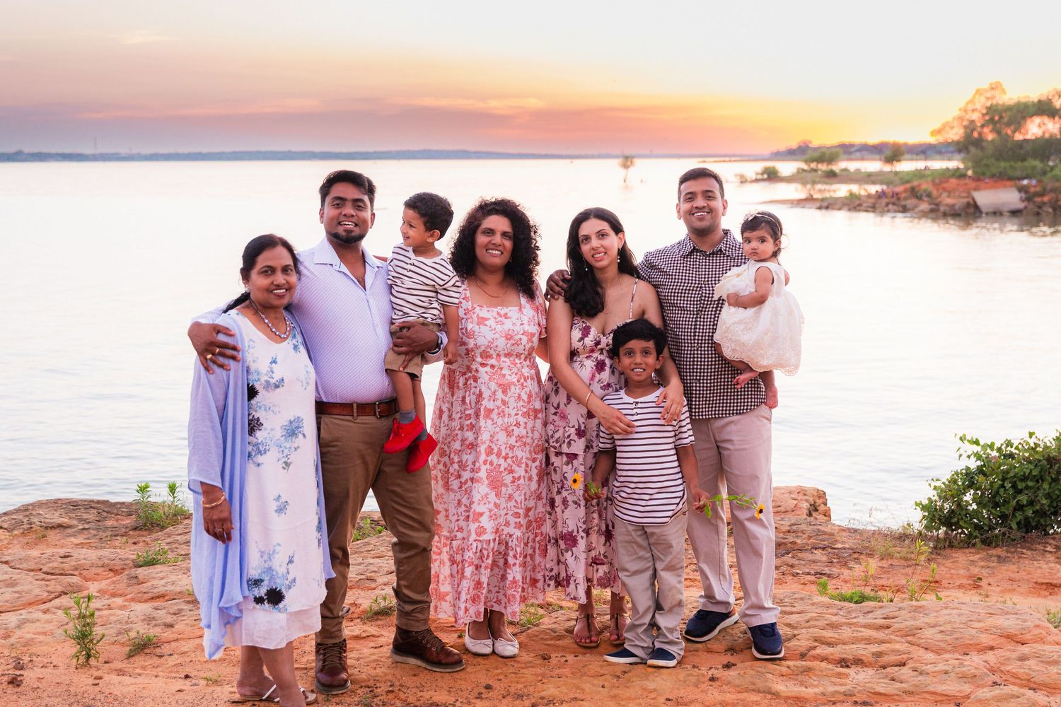 Family of seven posing together at sunset by a serene lakeside, smiling warmly in casual and festive attire.