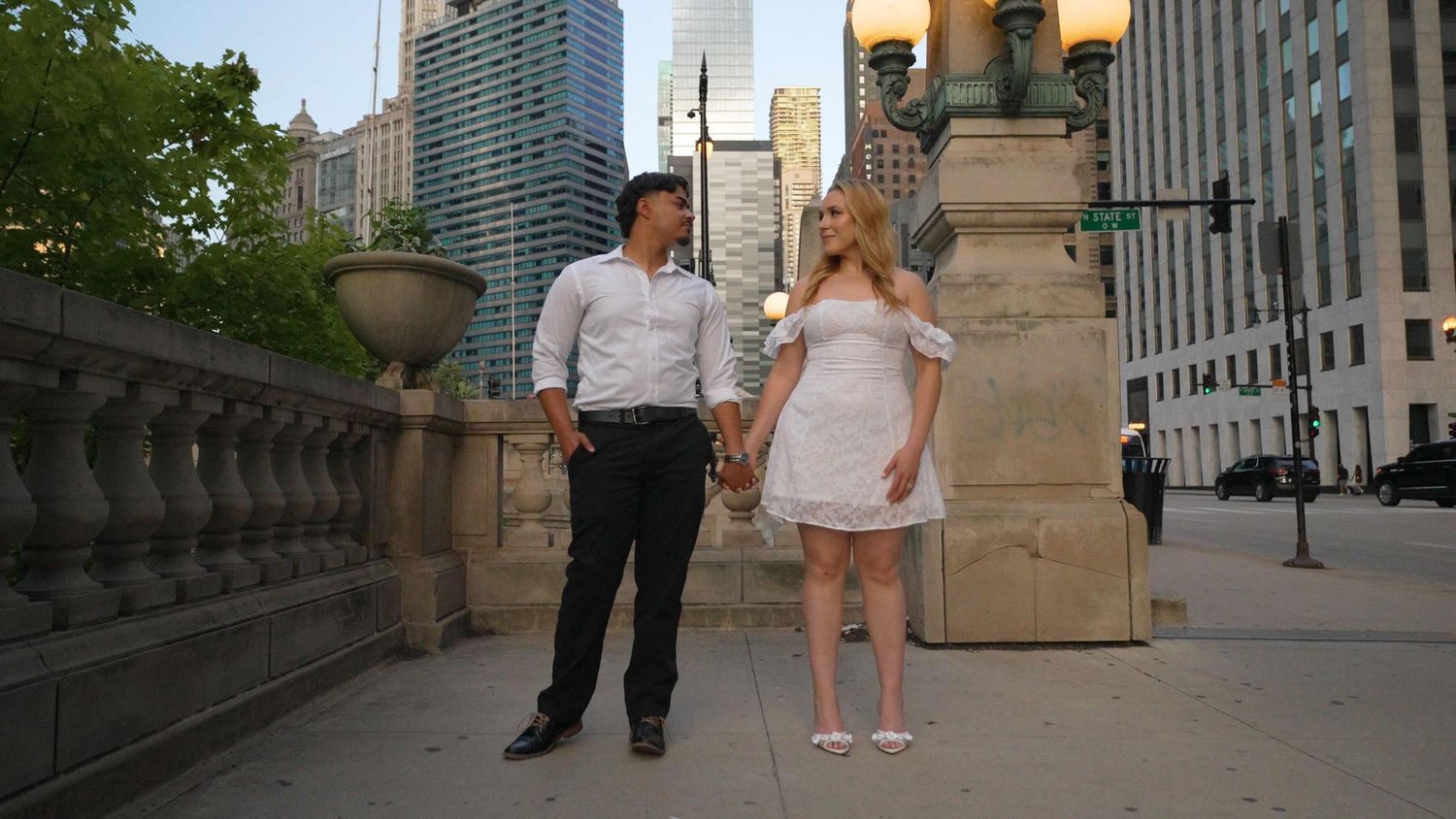 A young couple looking at each other in black & white formal attire above the Riverwalk in Downtown Chicago for an engagement video.