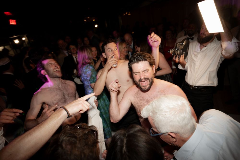 Energetic wedding reception dance floor with guests celebrating and dancing together in a dimly lit venue.