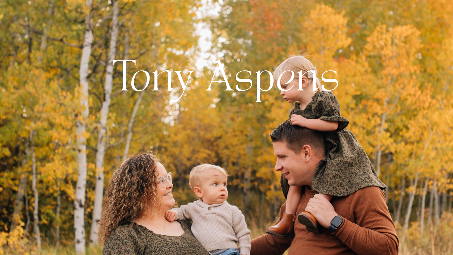Family posing among golden aspen trees in autumn, parents holding baby with fall foliage backdrop.