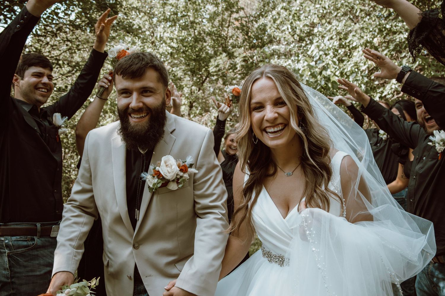 Newlyweds celebrate with guests during an outdoor wedding ceremony surrounded by blooming trees.