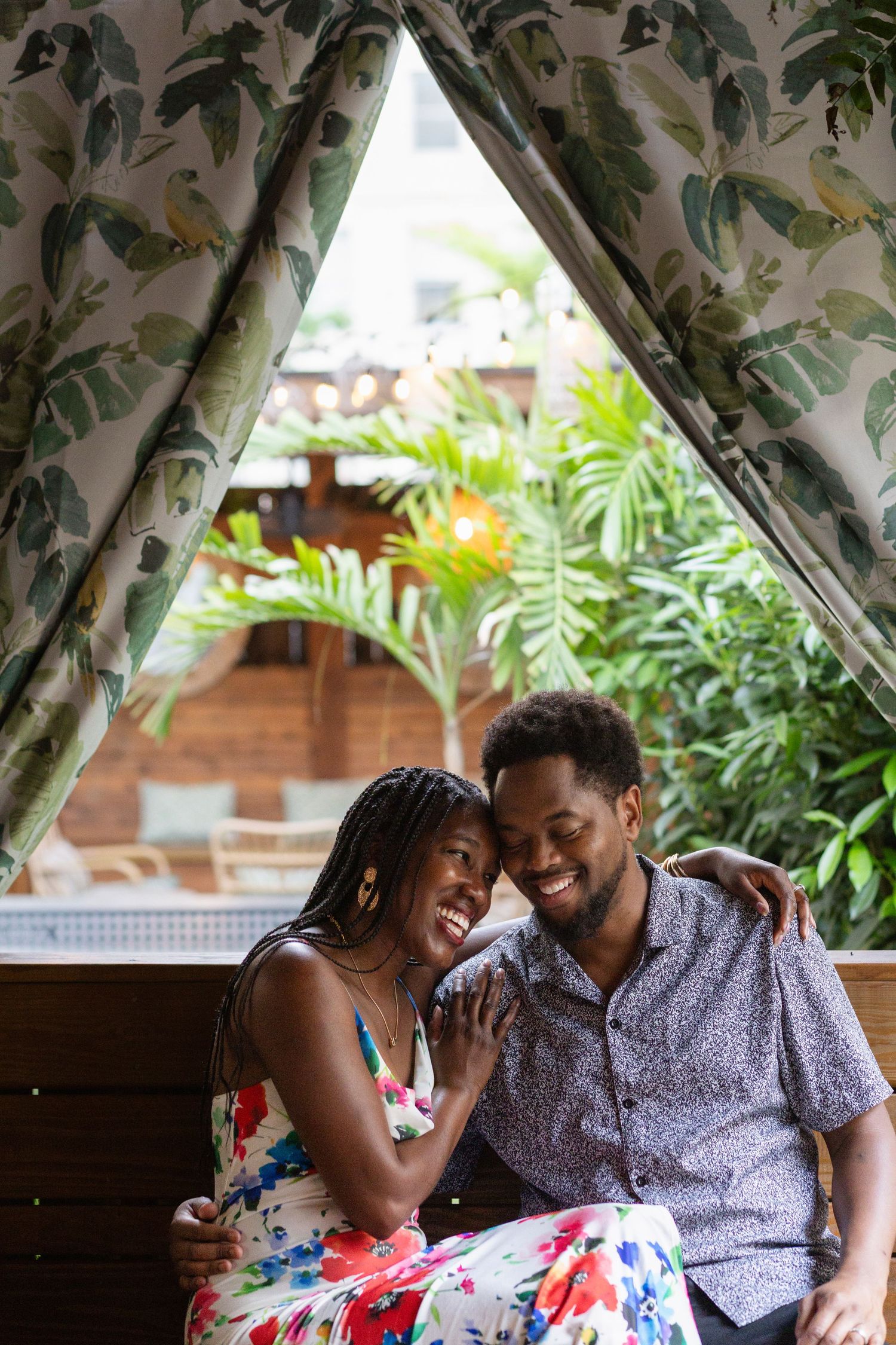 Cinematic couples portrait at The Grove on Main Street in Lexington smiling and embracing near tropical curtains and lush green plants.