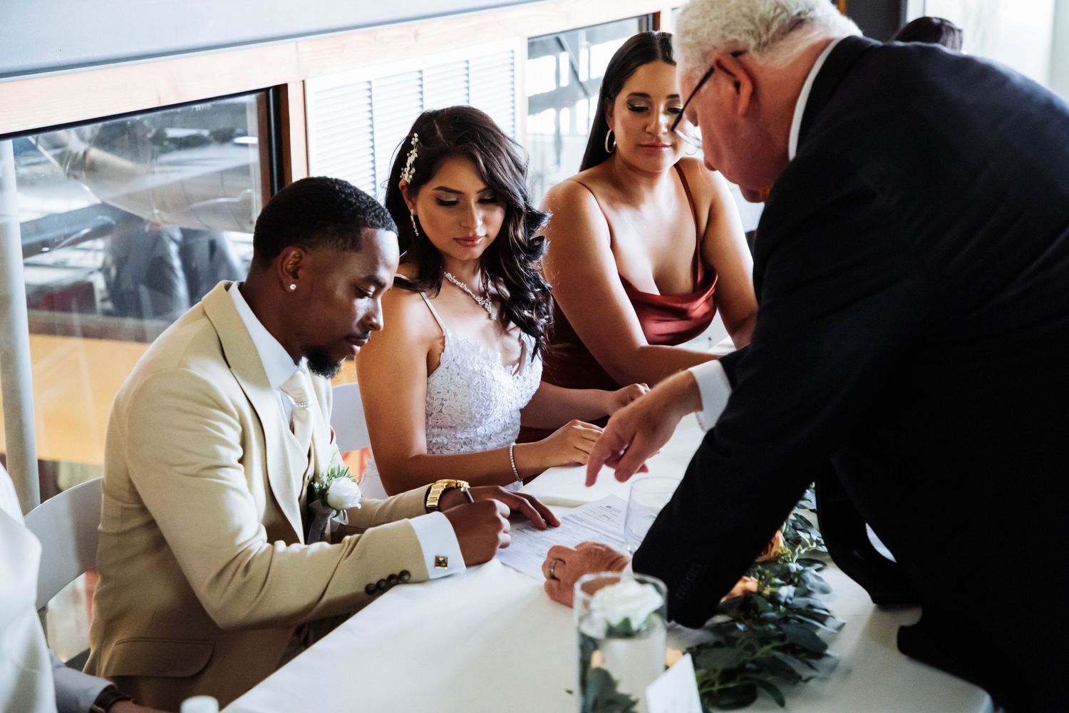Wedding couple signing documents with guests and officiant at ceremony.