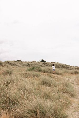 A child walks along a sandy coastal path surrounded by dune grasses during a family photography session in Sussex